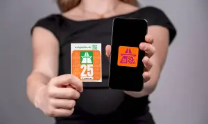 Ręce trzymają naklejkę i smartfon z aplikacją. Na naklejce widnieje napis "e-vignette.ch" i duża liczba "25", symbolizująca winietę szwajcaria.