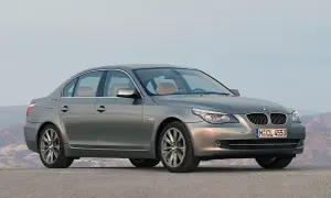Szary sedan BMW 5 E60 z jasnym wnętrzem stoi na pustej drodze, z górami w tle.