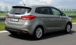 Szary Kia Carens 4 jedzie po drodze, w tle zielone pola i niebo.