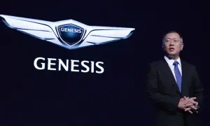 Mężczyzna w garniturze stoi obok logo Genesis, marki luksusowych samochodów.