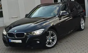 Eleganckie, czarne BMW 318d kombi na tle budynku. Lśniący lakier i nowoczesne felgi.