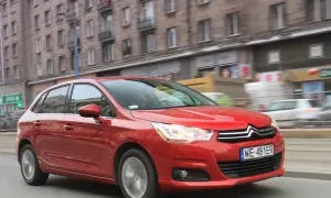 Czerwony Citroen C4 1.6 HDI w ruchu miejskim, z budynkami w tle.