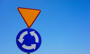Znak ustąp pierwszeństwa i znak informujący o ruchu okrężnym na tle błękitnego nieba.
