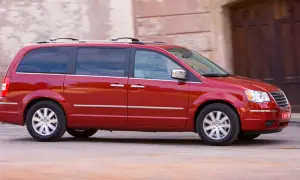 Czerwony Chrysler Grand Voyager w ruchu, z przyciemnianymi szybami i relingami dachowymi, przemierza ulicę.