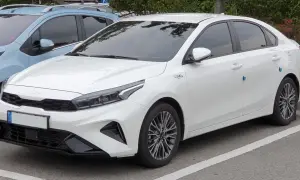 Biały sedan Kia Forte zaparkowany na parkingu, widok z przodu i z boku.