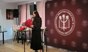 Kobieta przemawia na tle baneru z logo biblioteki, podczas wydarzenia w Garwolinie. Wgm rejestracja.