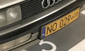Zbliżenie na przód samochodu Audi z charakterystycznym grillem i logo. Widoczne żółte tablice rejestracyjne z numerem NO 029.