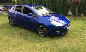 Błękitny Fiat Bravo 1.4 T-Jet zaparkowany na trawniku, za nim żywopłot.