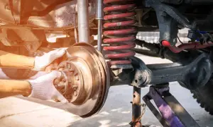 Mechanik w białych rękawiczkach wymienia tarczę hamulcową przy skomplikowanym wielowahaczu terenowego pojazdu.