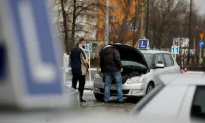 Dwóch mężczyzn przy samochodzie z otwartą maską, znaki "L" i numery na placu manewrowym.