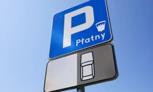 Znak D18 informuje o płatnym parkingu. Widoczny jest symbol samochodu na tablicy pod znakiem.