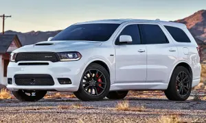 Biały Dodge Durango 3.6 SRT z czarnymi felgami i czerwonymi zaciskami hamulcowymi stoi na żwirowej drodze, w tle góry i opuszczony dom.