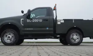 Ciemnozielony Ford F350 z platformą, numerem SL-20010 i pomarańczowym kogutem na dachu.