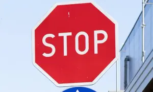 Czerwony znak stop z białym napisem "STOP" na tle błękitnego nieba i nowoczesnego budynku.