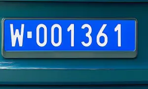 Niebieskie tablice rejestracyjne z numerem W-001361 na ciemnozielonym samochodzie.