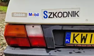 Tył białego samochodu Skoda z naklejkami "Mobil" i "Szkodnik". Widoczna tablica rejestracyjna KWI.