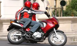 Dwie osoby w czerwonych kaskach i kurtkach jadą na czerwonym motocyklu. To świetna kategoria a1 dla miłośników wolności.