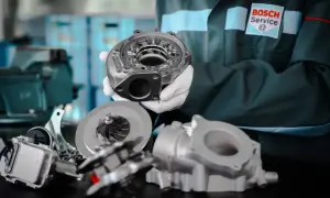 Mechanik w białych rękawiczkach prezentuje części turbosprężarki biturbo.