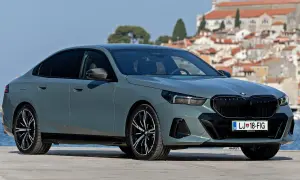 Nowe BMW Serii 5 w kolorze szarym, zaparkowane na tle malowniczego miasta nad morzem.