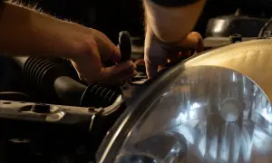Ręce mechanika, jak pracowity knecht, przykręcają reflektor samochodu.