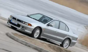 Srebrny Mitsubishi Galant z kierowcą za kierownicą, pokonujący zakręt na drodze.