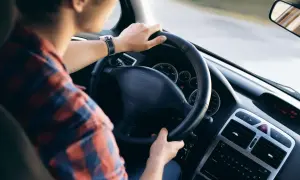 Mężczyzna w kratę prowadzi samochód. W tle widać deskę rozdzielczą i lusterko. To dobry moment na rozważenie amortyzacji samochodu używanego.