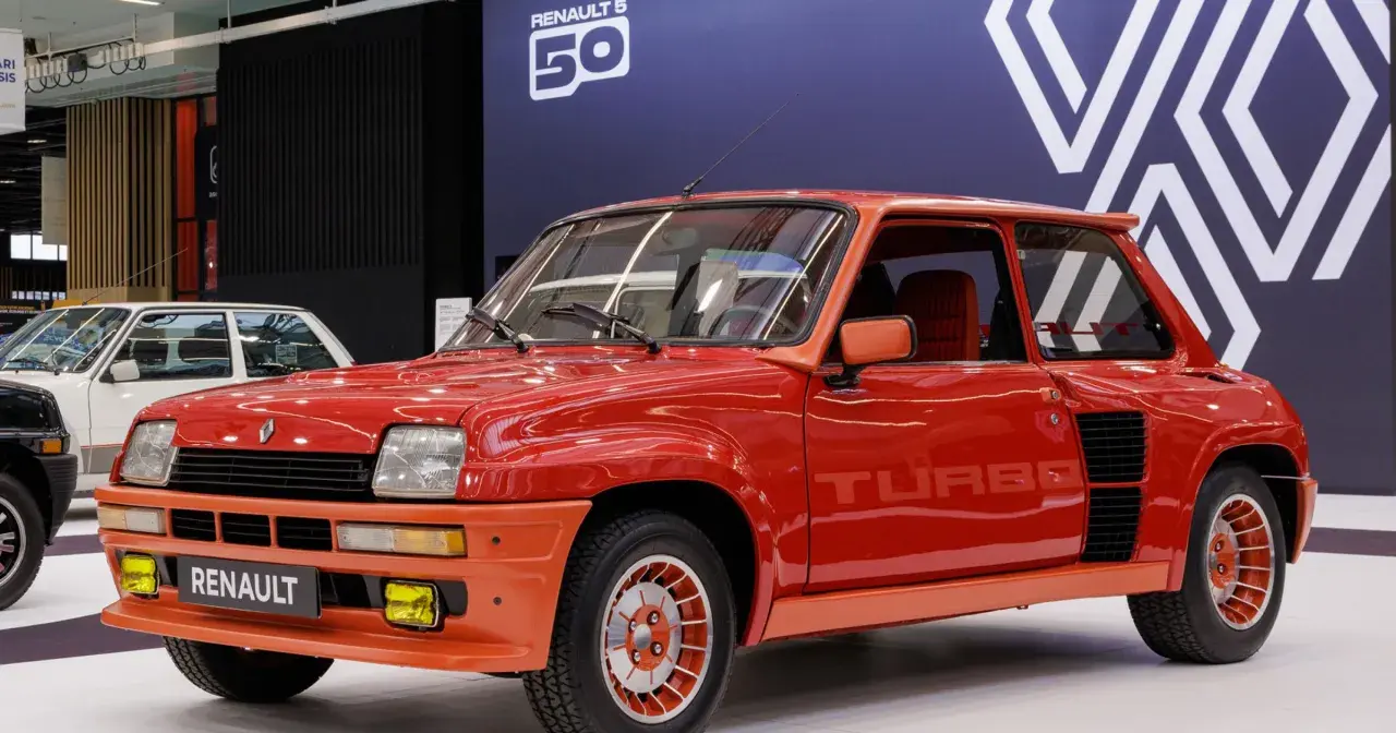 Czerwony Renault 5 Turbo z lat 80. błyszczy na wystawie. Charakterystyczne logo "TURBO" na drzwiach i pomarańczowe akcenty podkreślają jego sportowy charakter.