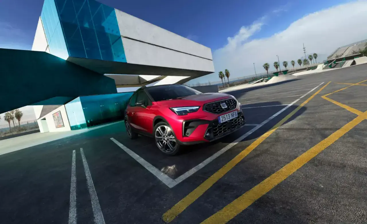 Czerwony SUV SEAT Arona, jeden z najnowszych seat modele, zaparkowany przy nowoczesnym budynku z niebieskimi akcentami.