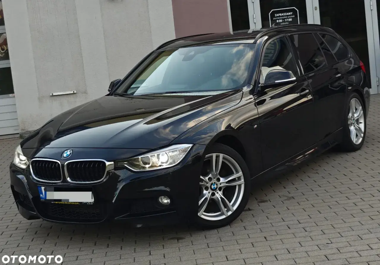 Eleganckie, czarne BMW 318d kombi na tle budynku. Lśniący lakier i nowoczesne felgi.
