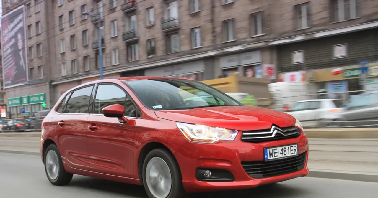 Czerwony Citroen C4 1.6 HDI w ruchu miejskim, z budynkami w tle.