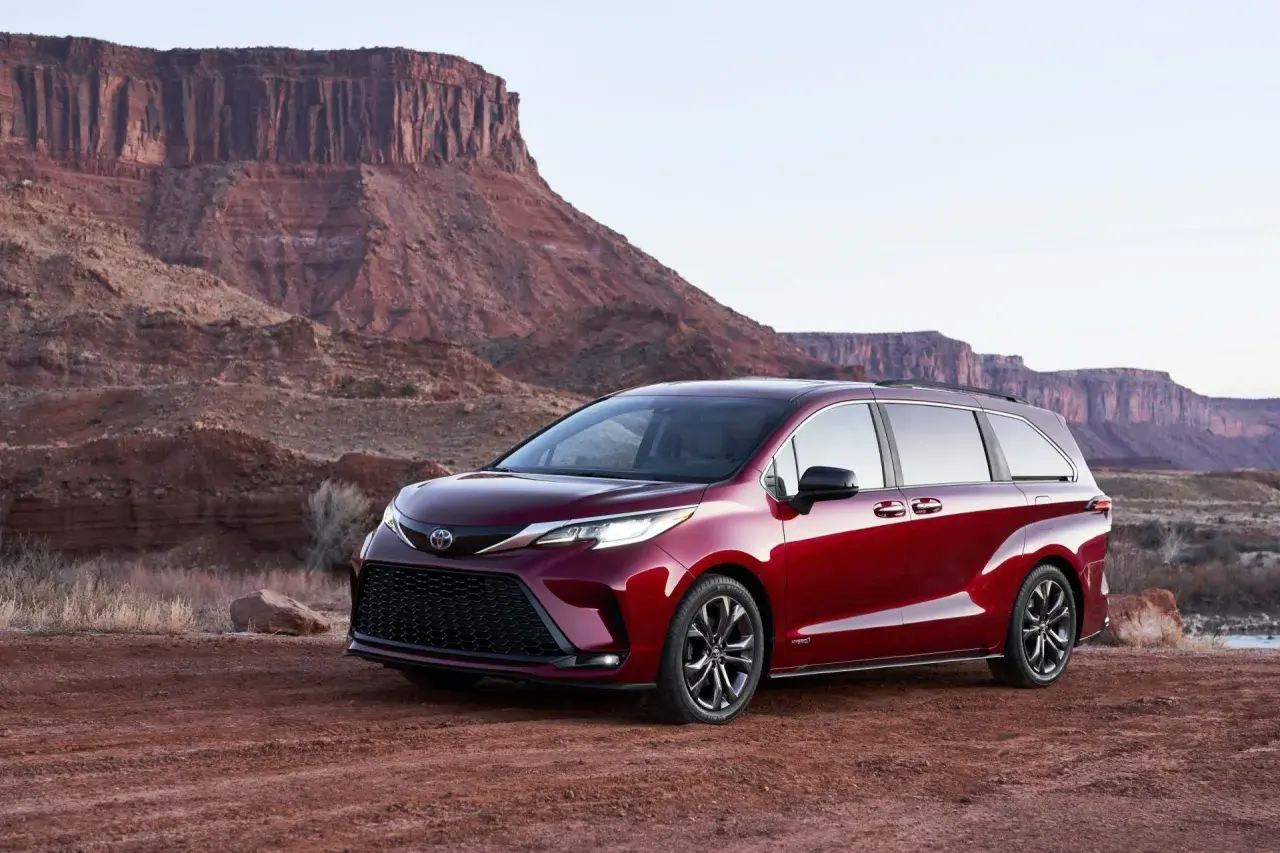 Czerwony minivan Toyota Sienna Hybrid na tle pustynnego krajobrazu z klifami.