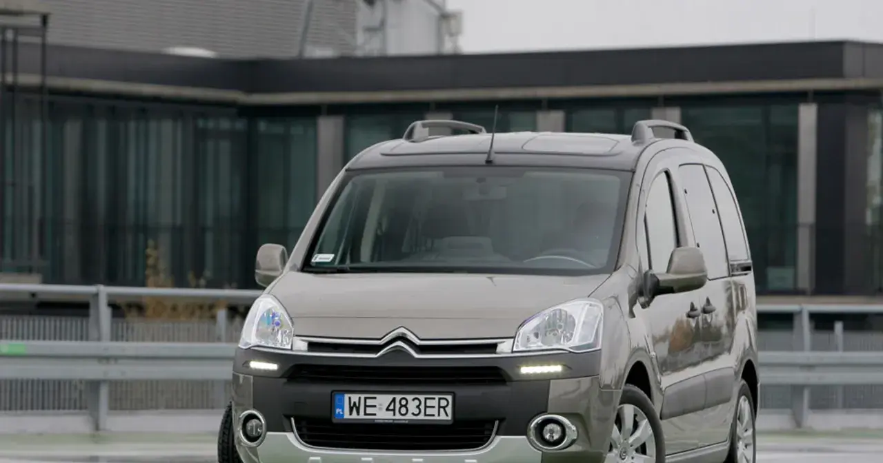 Szary Citroen Berlingo 1.6 HDI z relingami dachowymi zaparkowany przed nowoczesnym budynkiem.