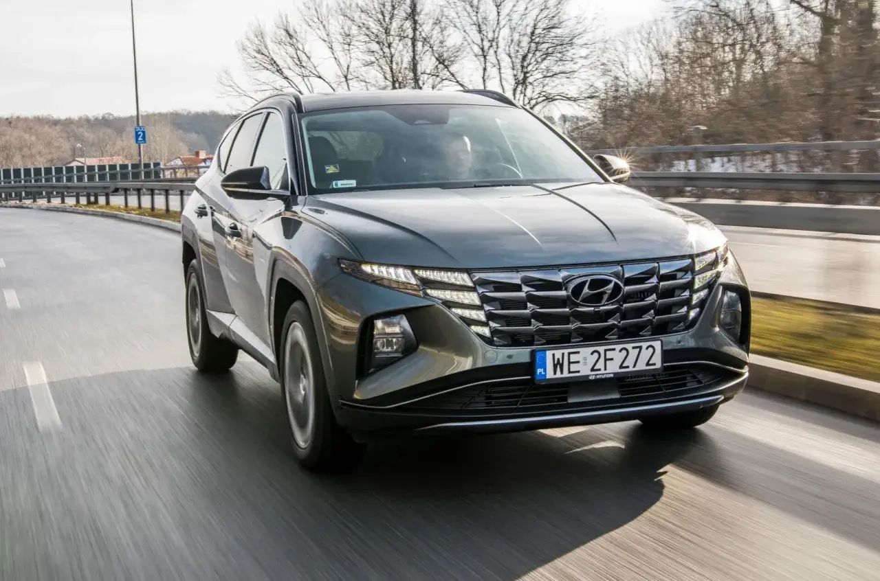 Szary Hyundai Tucson 1.6 T-GDI w ruchu drogowym, z widocznym grillem i światłami LED.