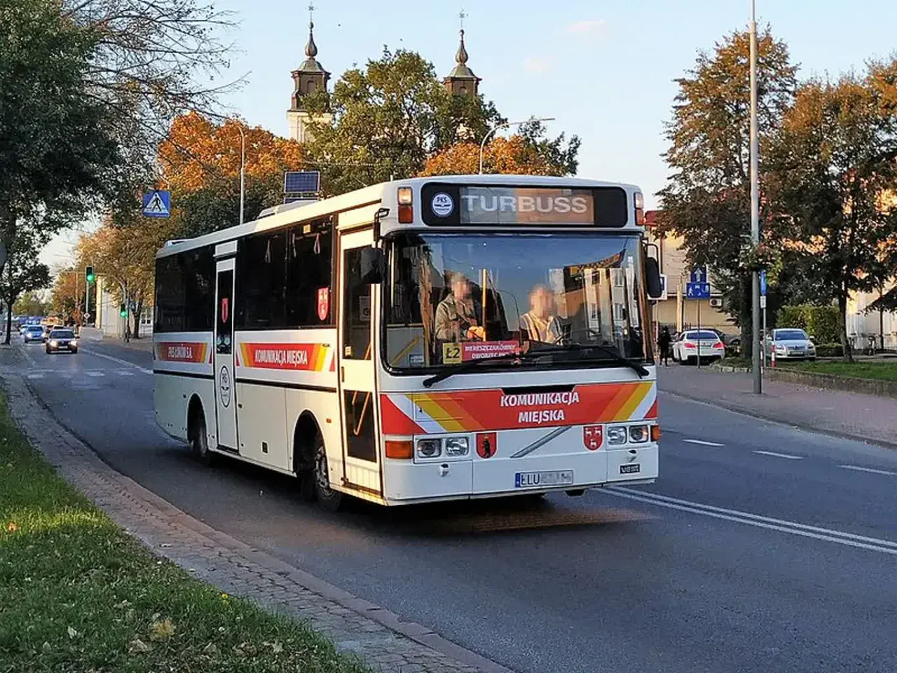 Autobus komunikacji miejskiej z napisem "TURBUSS" na tablicy kierunku, na ulicy w jesienny dzień. Rejestracja ELU.