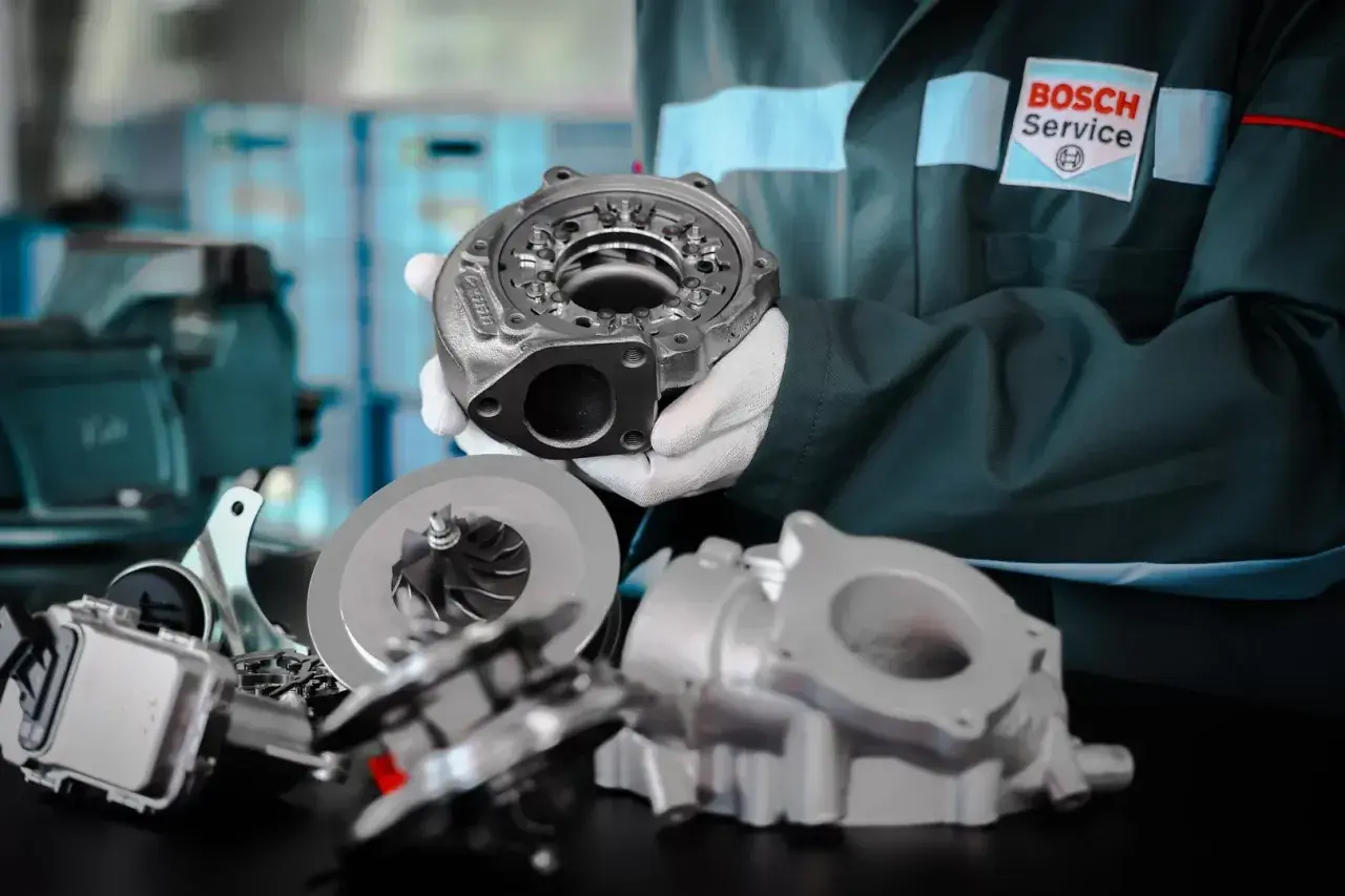 Mechanik w białych rękawiczkach prezentuje części turbosprężarki biturbo.