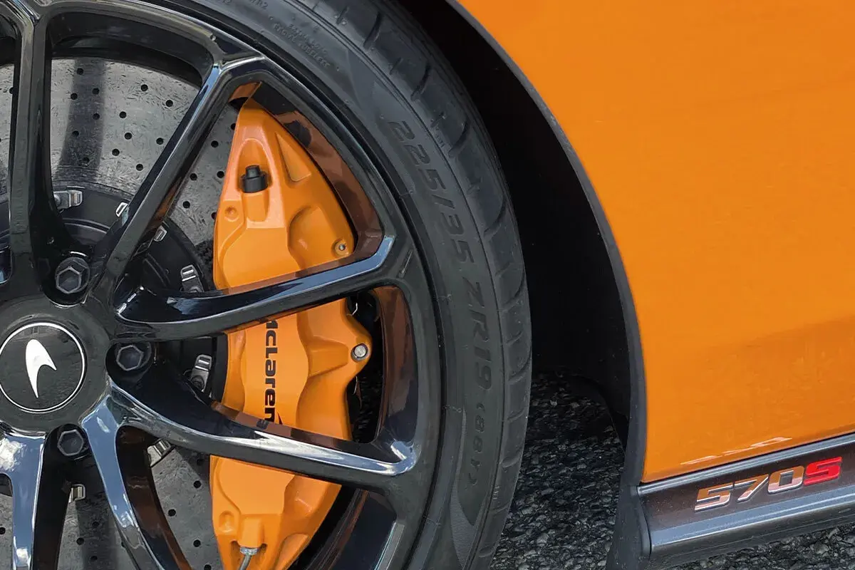 Pomarańczowy zacisk hamulcowy McLaren z oznaczeniami opon 225/35 ZR19 na czarnej feldze.
