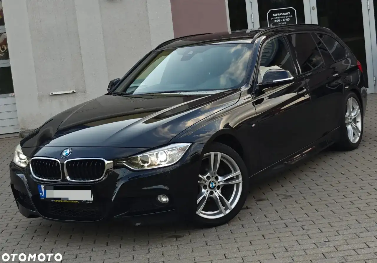 Eleganckie, czarne BMW 318d kombi na tle budynku. Lśniący lakier i nowoczesne felgi.