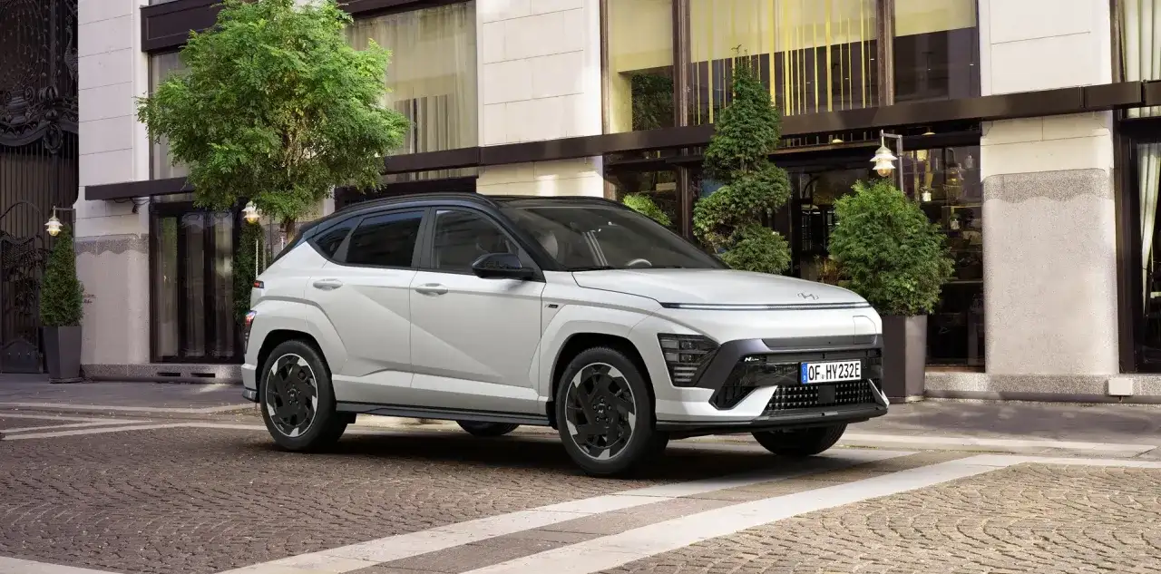 Nowy Hyundai Kona w białym kolorze, zaparkowany przed eleganckim budynkiem. Sprawdź atrakcyjną hyundai kona cena!