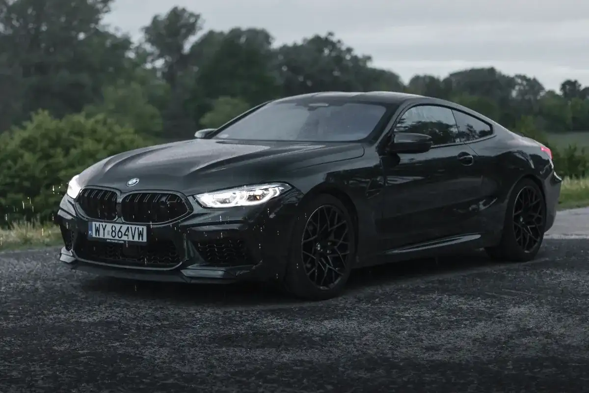 Mroczny BMW M8 na mokrej drodze. Zastanawiasz się nad jego ceną? Ten sportowy coupe robi wrażenie.