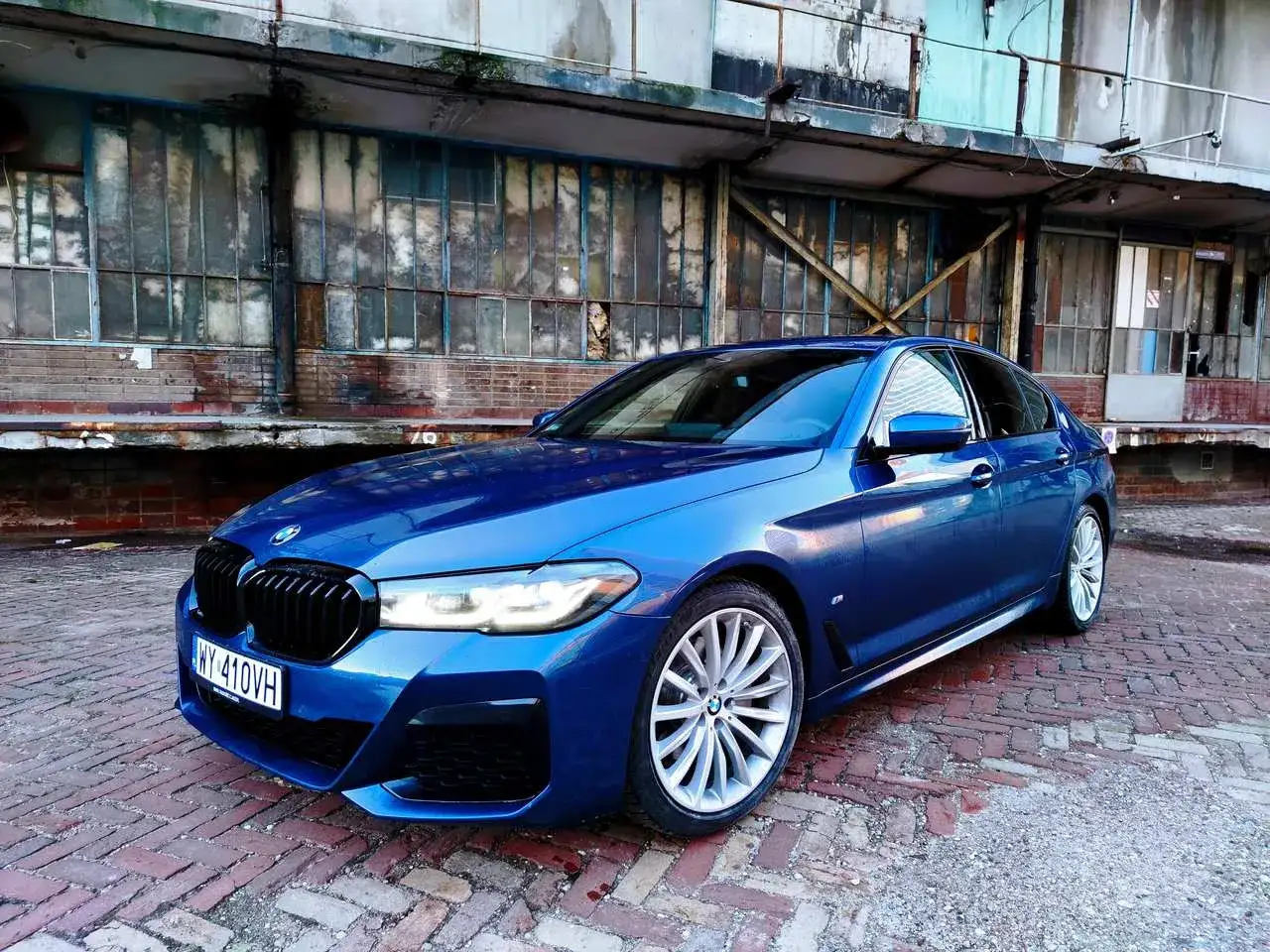 Błękitne BMW 520d xDrive na tle postindustrialnego budynku.