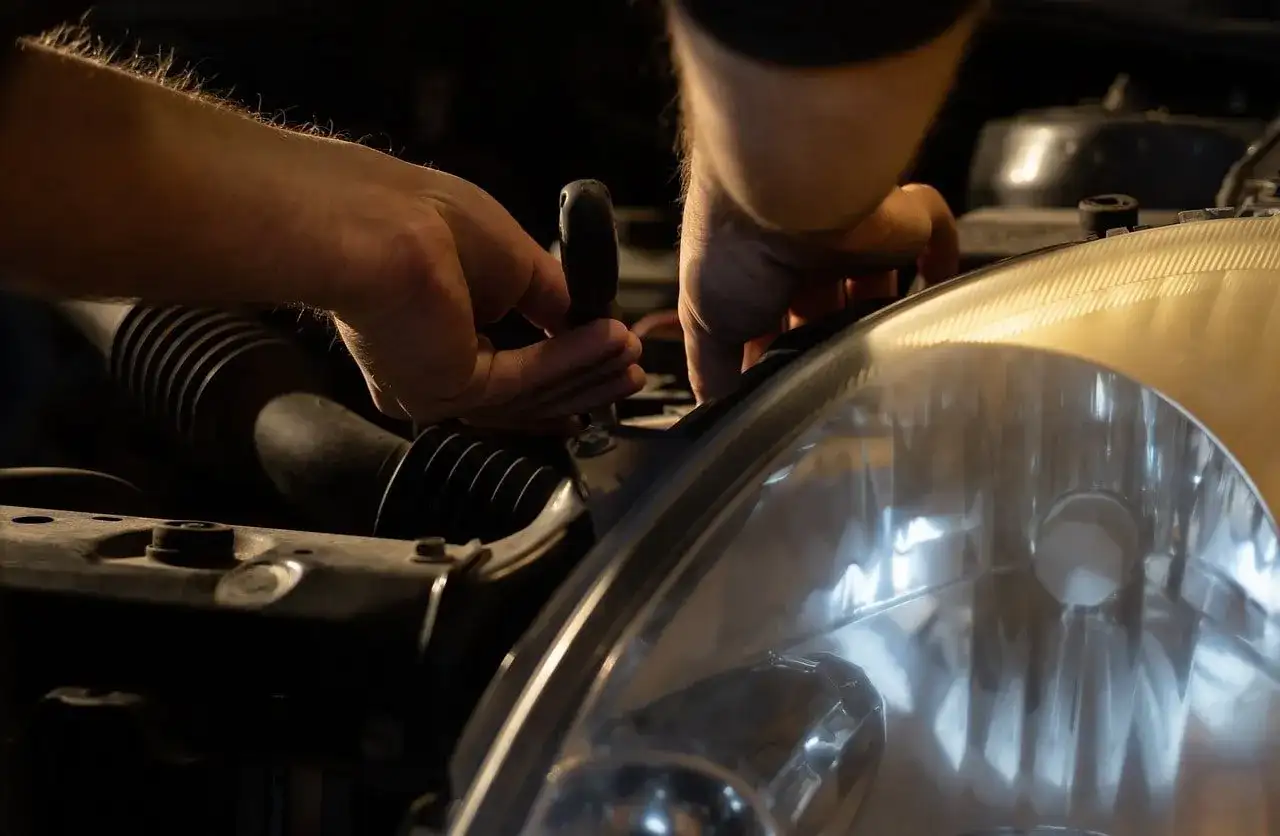 Ręce mechanika, jak pracowity knecht, przykręcają reflektor samochodu.