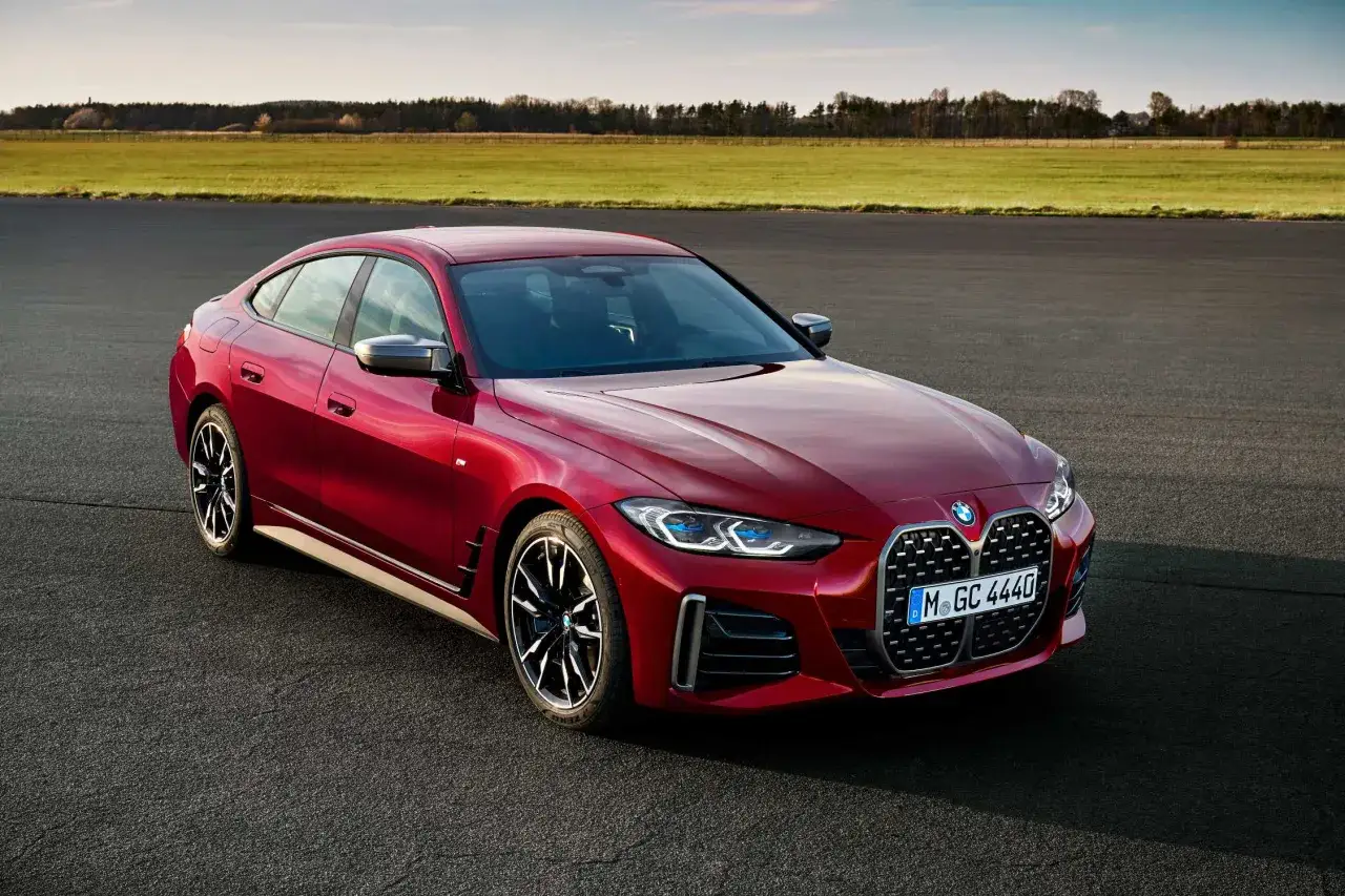 Czerwone BMW 4 Gran Coupé na tle zielonych pól i błękitnego nieba.