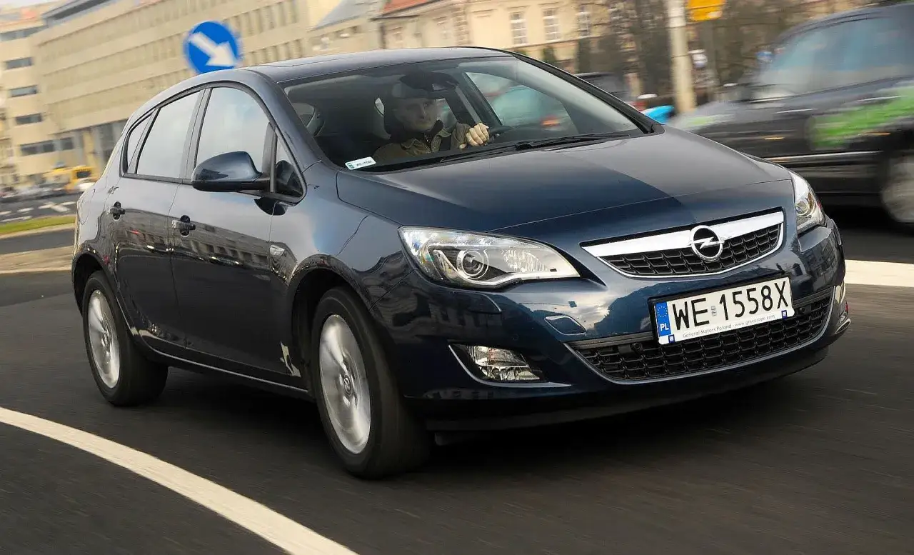 Ciemnoniebieski Opel Astra J 1.4 Turbo z polskimi tablicami WE 1558X jedzie po miejskiej drodze.