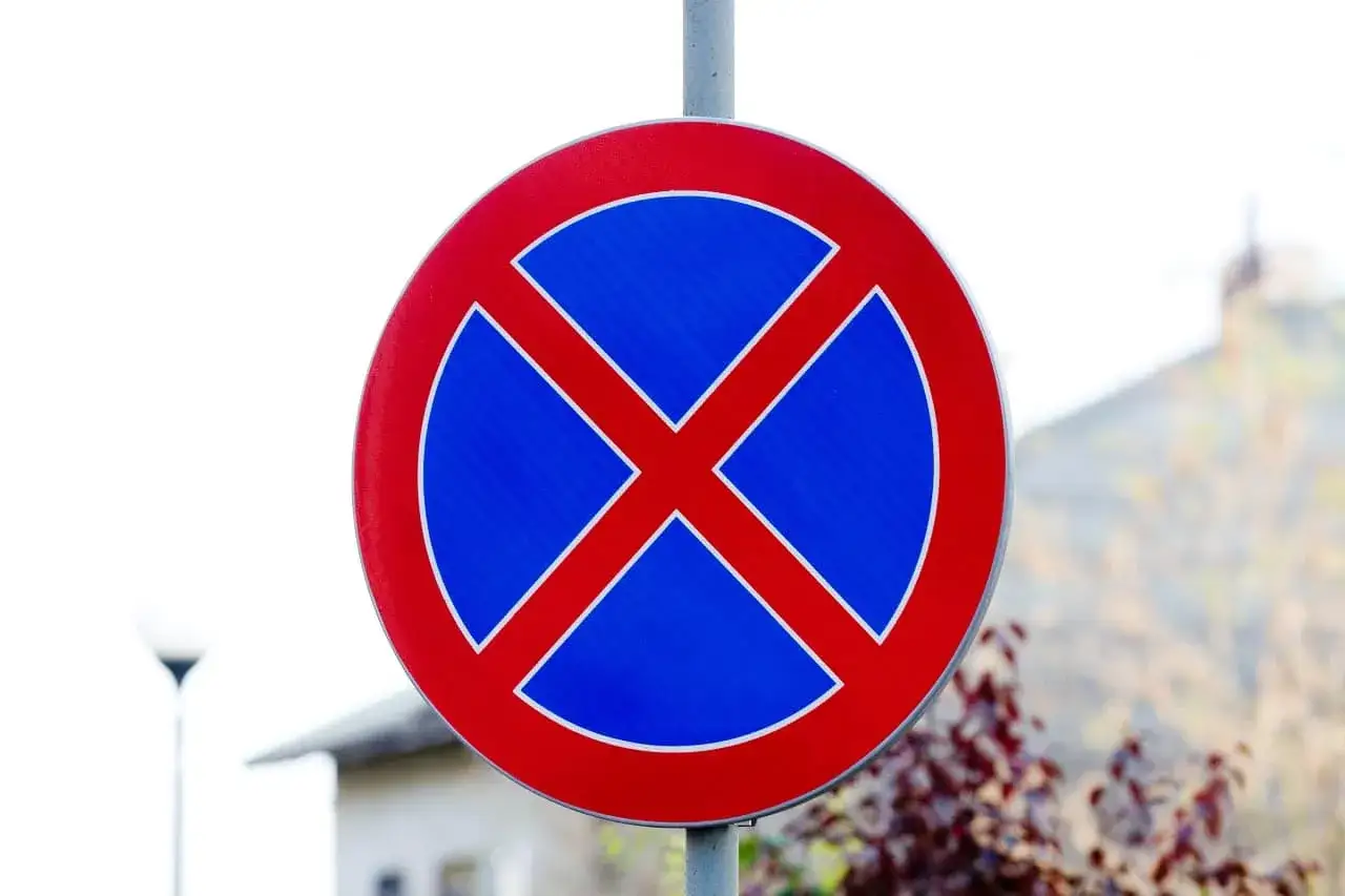 Znak drogowy informujący o zakazie postoju. Czerwone X na niebieskim tle ostrzega kierowców.