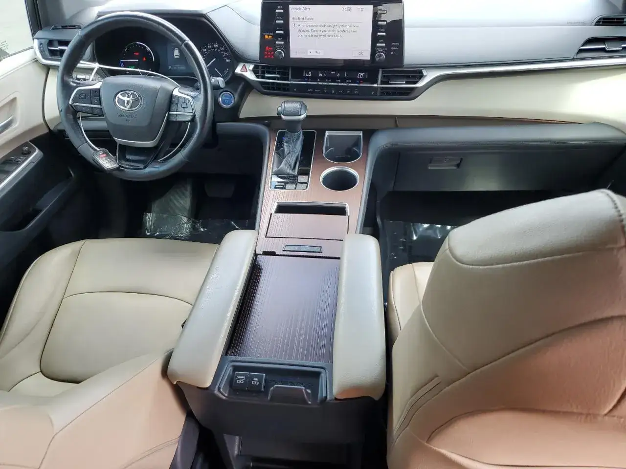 Wnętrze Toyoty Sienna Hybrid z jasnymi skórzanymi fotelami, ekranem multimedialnym i drewnianymi akcentami.