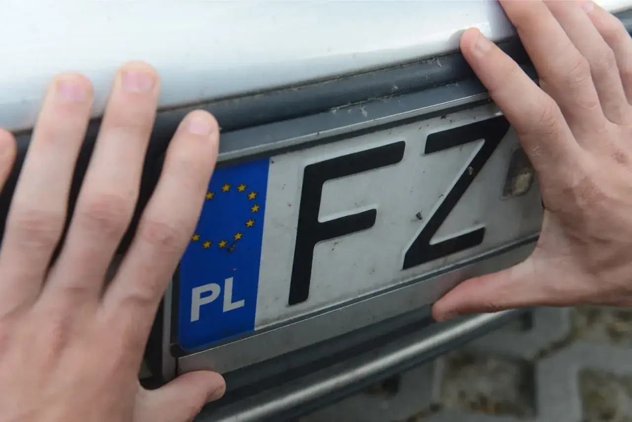 Dłonie trzymają tablicę rejestracyjną z literami FZ. LTM rejestracja w toku.