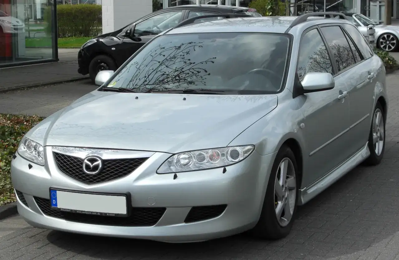 Srebrna Mazda 6 GG kombi zaparkowana na zewnątrz. Widać jej przednią część, reflektory i grill z logo.