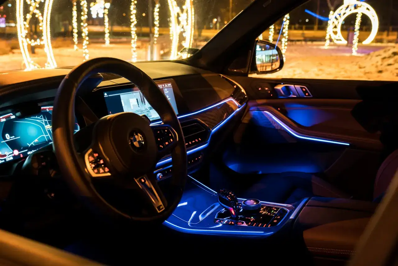 Wnętrze BMW X5 M50d nocą, z niebieskim nastrojowym oświetleniem i świątecznymi iluminacjami za oknem.