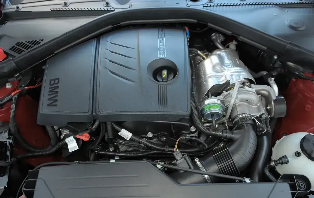Silnik TwinPower Turbo w BMW 116i. Widoczny czarny plastikowy dekiel z logo BMW i turbosprężarka.