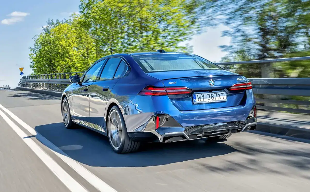 Błękitne BMW 520d xDrive pędzi po drodze, otoczone zielenią drzew.